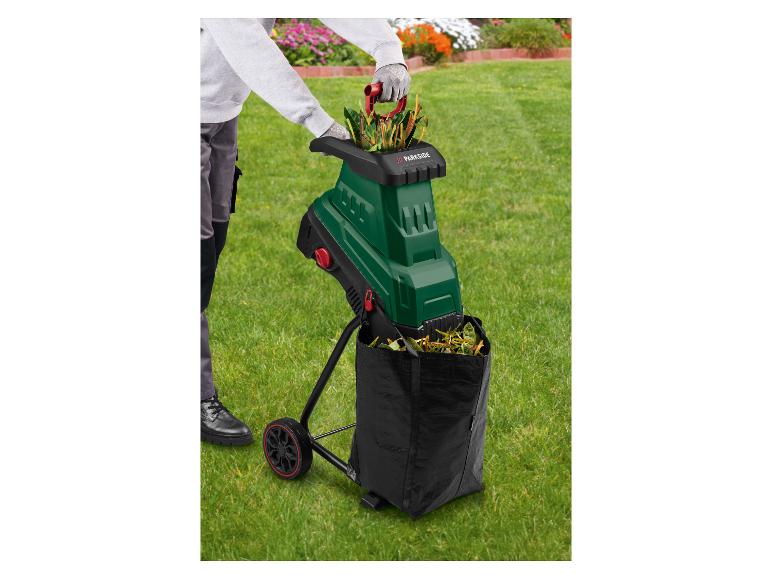 Persoon in de tuin gebruikt een groene tuinhakselaar met een zwarte opvangzak.