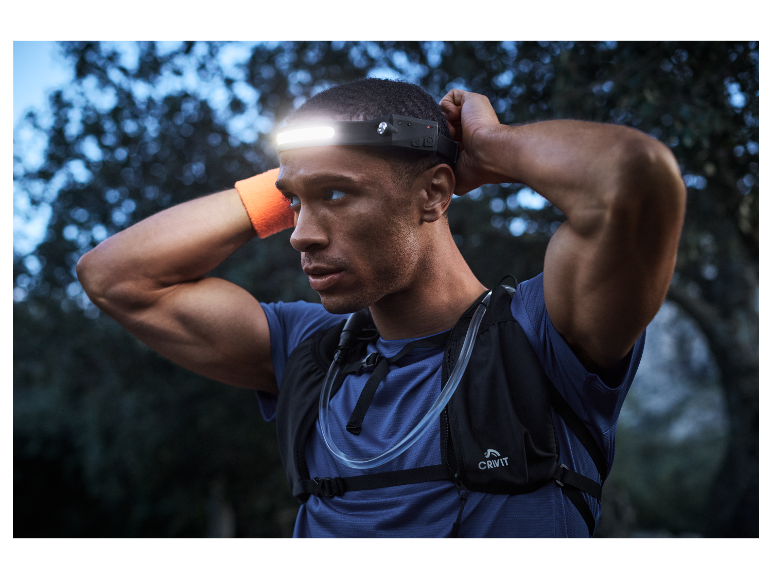 Een man met een CRIVIT hardloopvest en hoofdlamp traint buiten in de schemering.