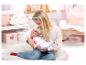 Een meisje houdt een Baby Born pop vast op een ronde kussen.