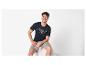 Man in een donkerblauw T-shirt met de tekst „ATHLETIC 1973 BLUE DIVISION” en grijze shorts.