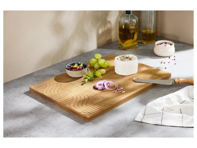 Een houten snijplank met kaas, druiven, rode ui en een klein kommetje jam.