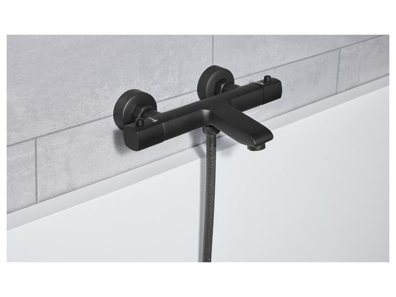 Een zwarte matte badkraan met douchekop is gemonteerd op een grijze betegelde wand.