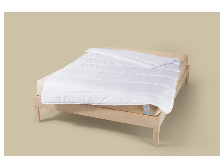 Wit dekbed op een licht houten bedframe met een beige hoeslaken.