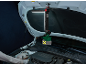 LED-werklamp met accu hangt onder open motorkap van auto, persoon controleert motor.