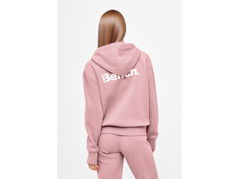 Vrouw in een roze hoodie en joggingbroek, met witte tekst op de rug.