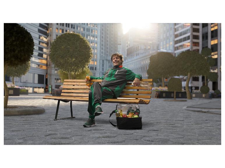 Man in trainingspak op een parkbankje met een koeltas vol vers fruit en een drankje.