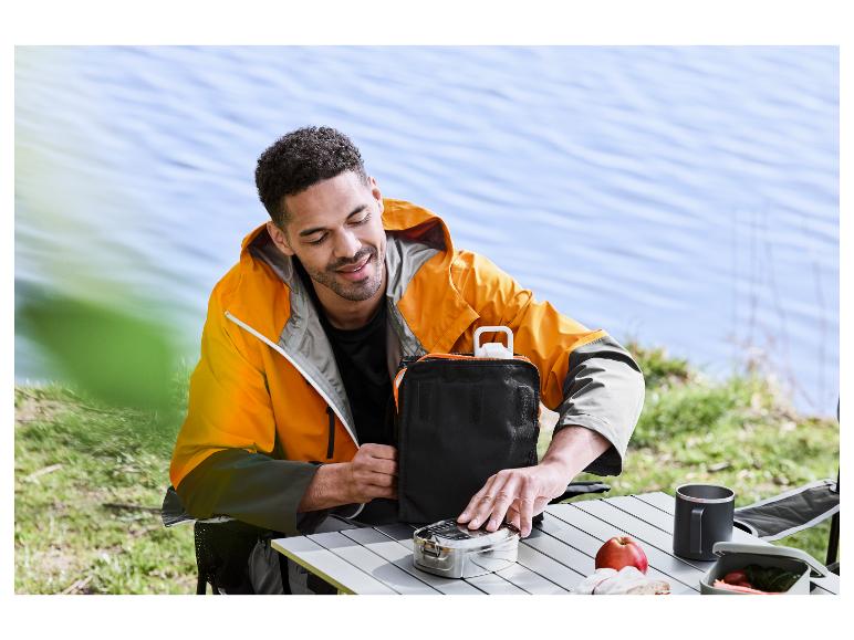 Man pakt lunchbox uit bij het meer.