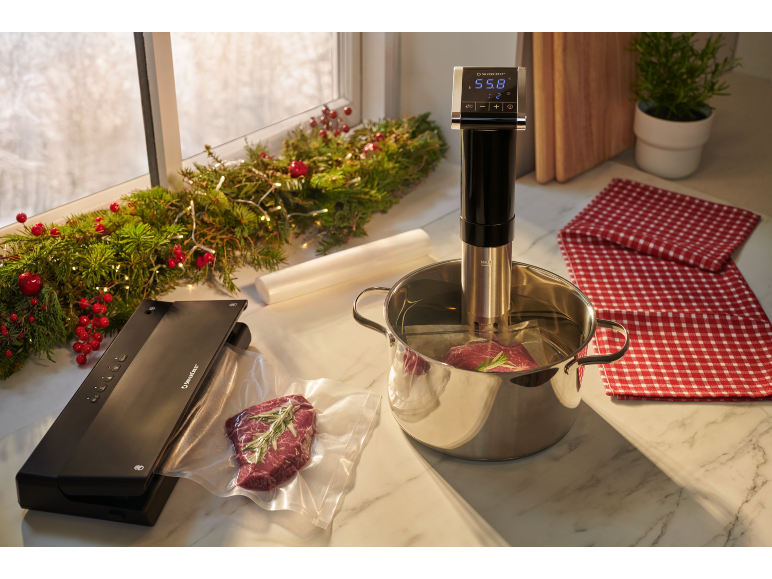 Sous-vide en vacuümsealer met vlees, kerstdecoraties en geruite theedoeken.