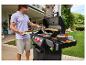 Man grilt hamburgers op een buitenbarbecue, met broodjes en groenten klaar.