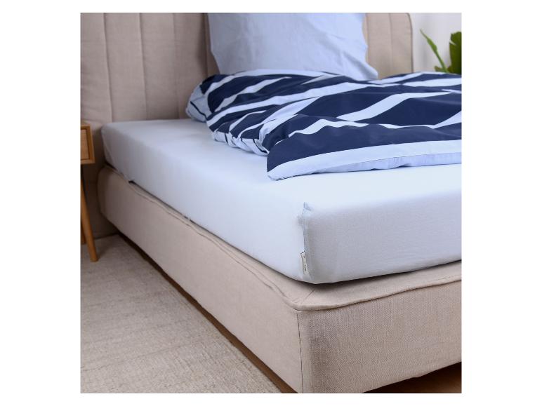 Bed met een wit hoeslaken en een blauw gestreept dekbed.