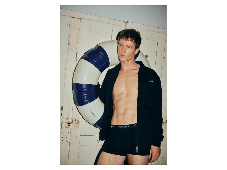 Man zonder shirt in open jasje en boxershorts, met een reddingsboei.