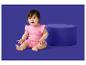 Een baby in een roze romper met zonnepatroon zit naast een blauwe poef.