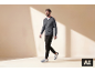 Man in een grijze V-hals trui, zwarte broek en witte sneakers loopt.