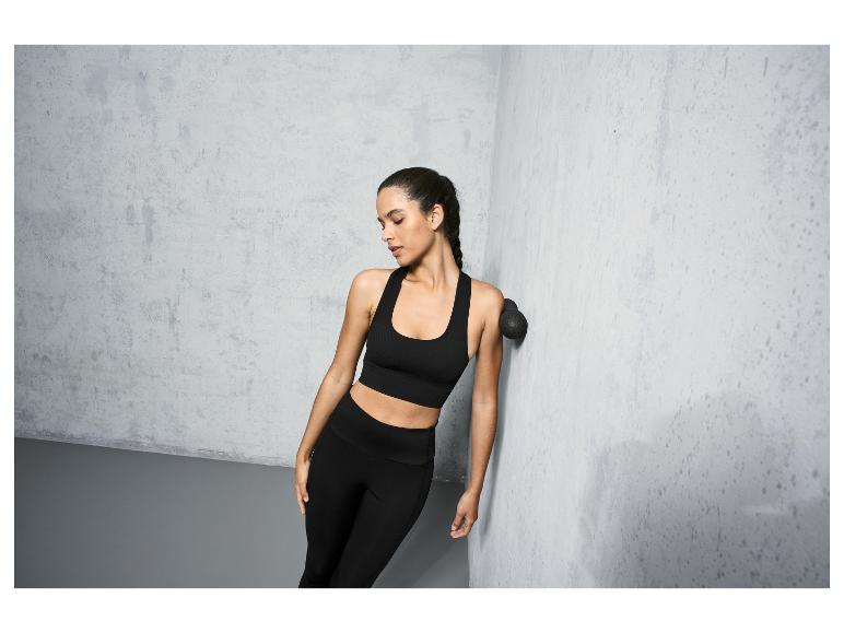 Een vrouw in zwarte sportkleding gebruikt een massagebal tegen een betonnen muur.