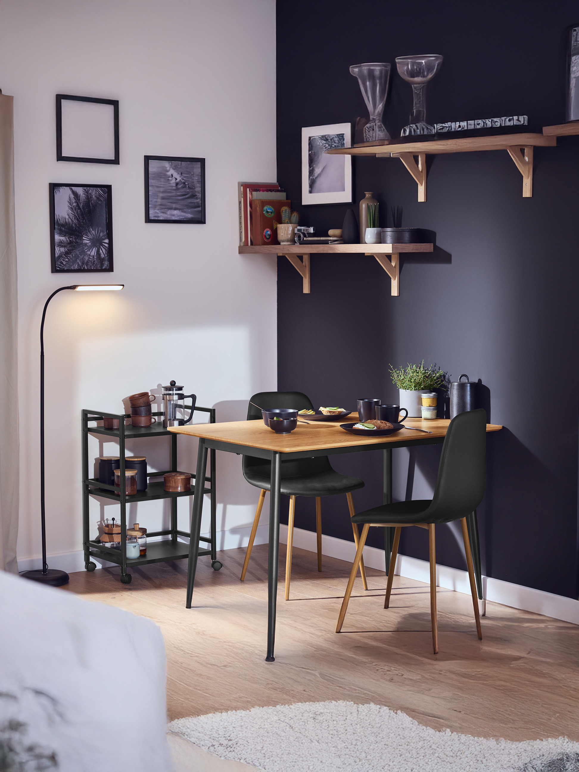 Eetkamer met houten tafel, zwarte stoelen, serveerwagen en planken met decoratie.