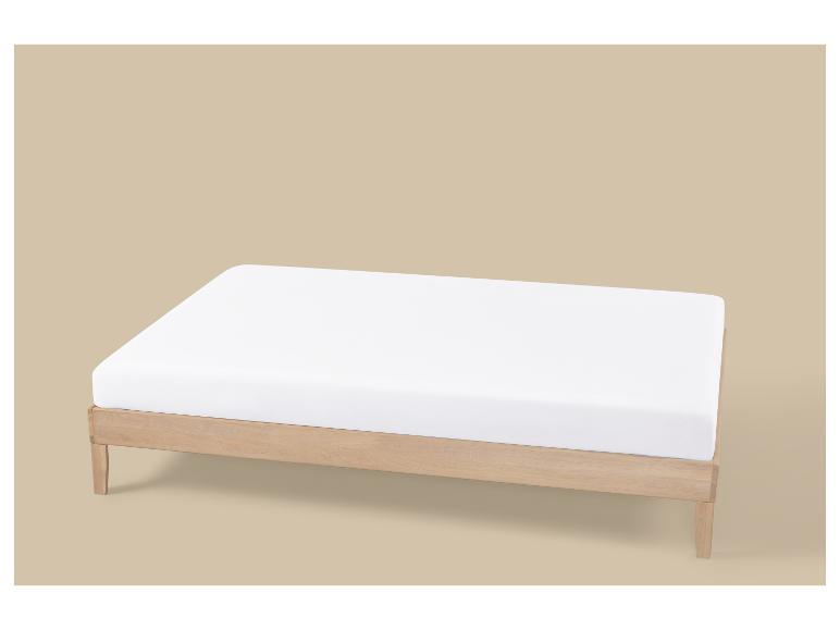 Licht houten bedframe met een wit matras op een beige achtergrond.