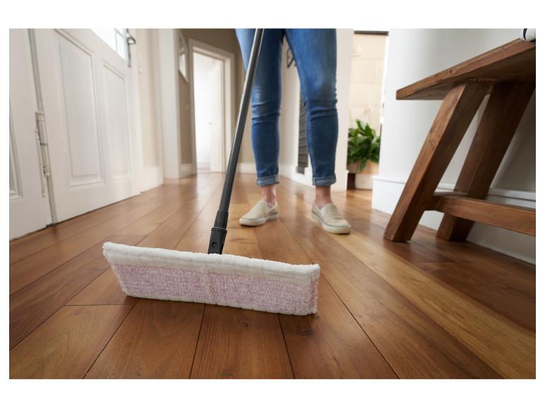 Een vrouw maakt een houten vloer schoon met een mop.