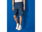 Een man draagt blauwe denim shorts met een Lidl-logo en witte sneakers.