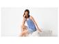 Vrouw in blauwe shorts en top zit lachend op een witte poef.