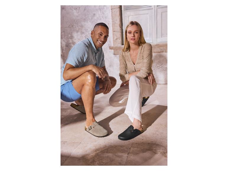 Man en vrouw in casual zomerkleding, klompen dragend, gehurkt op een tegelvloer.