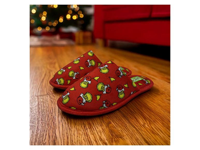 Rode Grinch-pantoffels op een houten vloer, met kerstverlichting op de achtergrond.