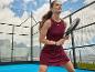Vrouw in sportjurk met padelracket op een buitenbaan.
