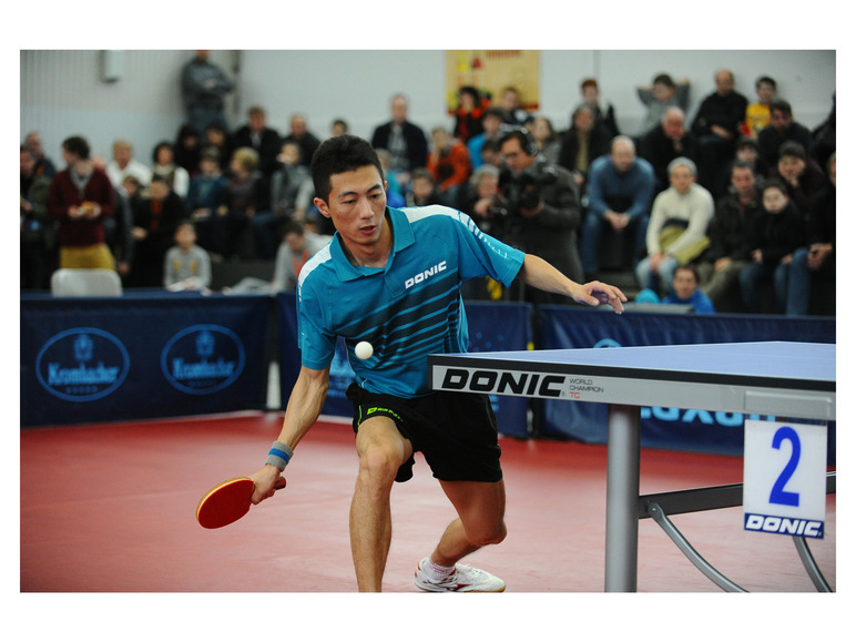 Een tafeltennisspeler in een blauw Donic shirt slaat de bal.