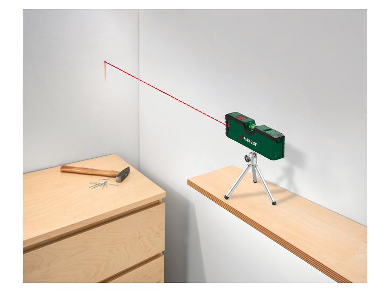 Groene laserwaterpas met statief projecteert rode lijn op muur, met hamer en spijkers.