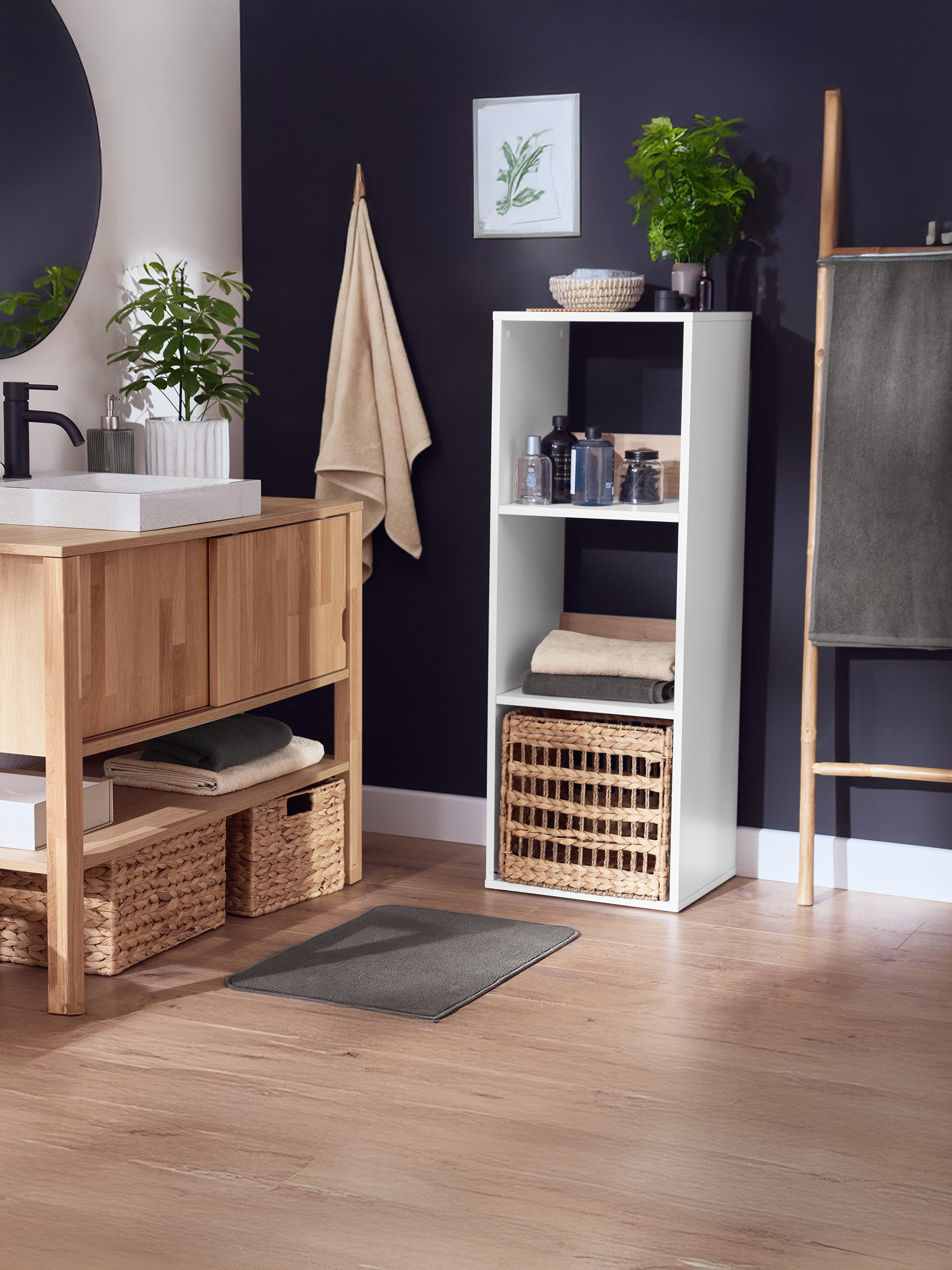 Badkamer met houten wastafelmeubel, spiegel, witte opbergkast en handdoekenrek.