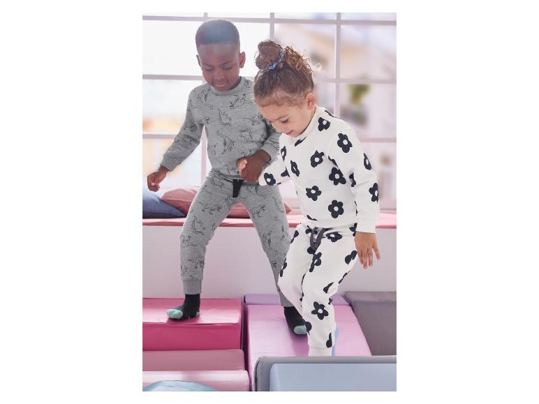 Twee kinderen spelen op zachte blokken, gekleed in pyjama's met print.