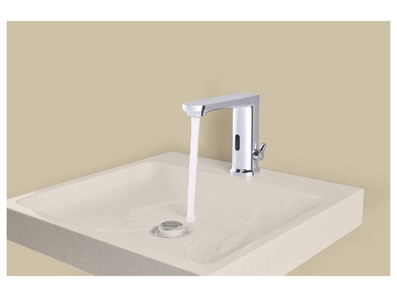 Chromen automatische kraan met stromend water in een lichte wastafel.