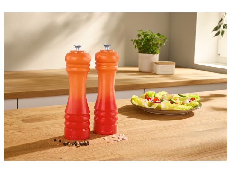Oranje peper- en zoutmolens op een houten aanrecht met een salade.