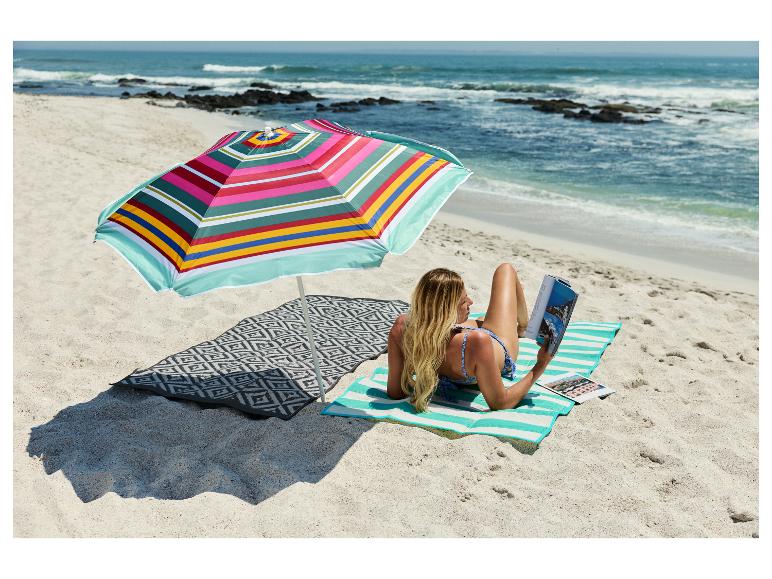 Vrouw leest onder een kleurrijke strandparasol op een gestreepte mat aan zee.
