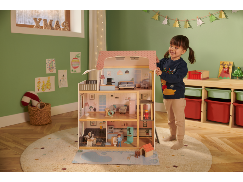 Een kind speelt met een groot houten poppenhuis in een feestelijke kamer.