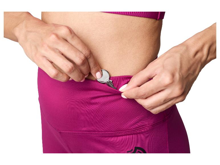 Vrouw stopt een sleutel in de verborgen zak van haar magenta sportlegging.