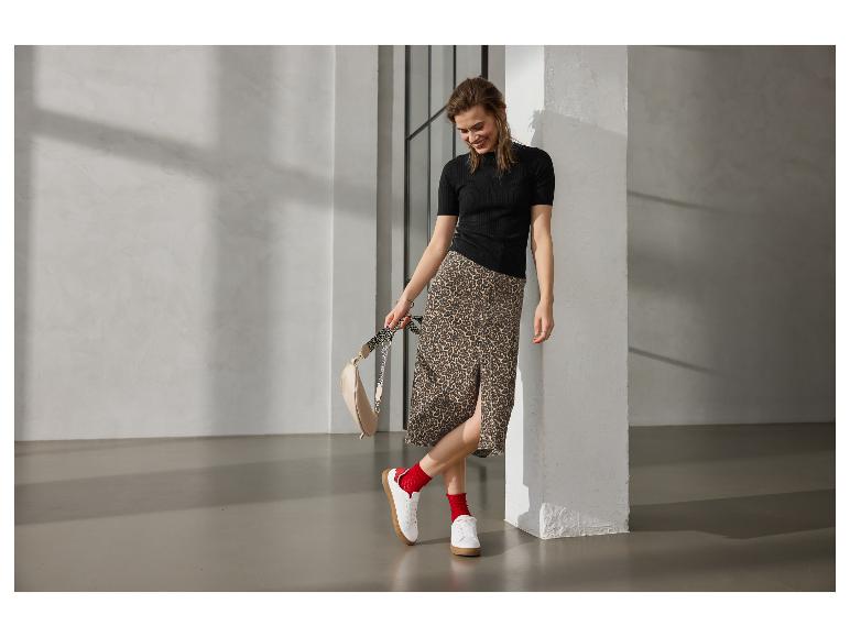 Vrouw in zwarte blouse, luipaardrok, rode sokken en witte sneakers, met tas.
