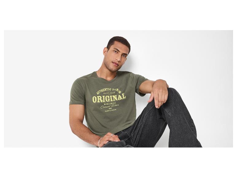 Man in een kakigroen T-shirt met „AUTHENTIC DENIM ORIGINAL”-opdruk en zwarte jeans.