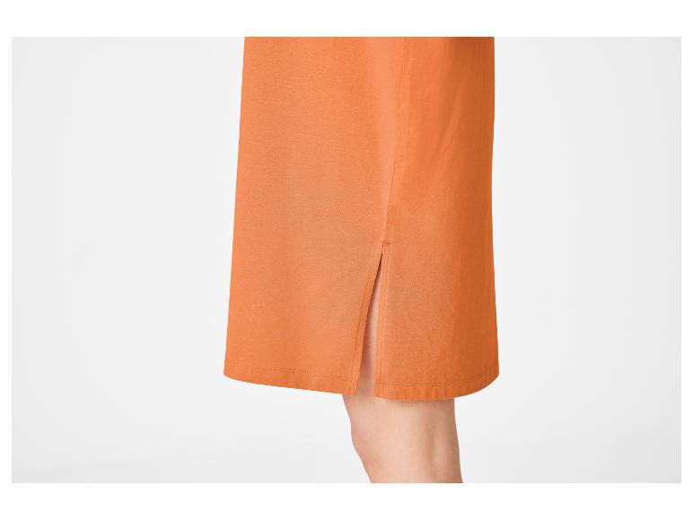 Detail van een oranje rok met zijsplit, toont een deel van een been.
