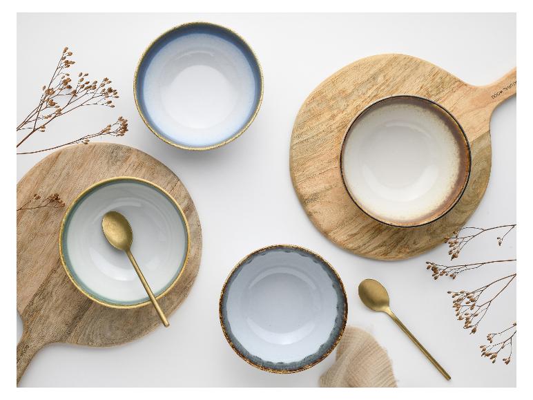 Vier keramische kommen op houten planken met lepels en gedroogde takken.