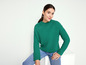 Een vrouw in een groene trui en blauwe jeans.