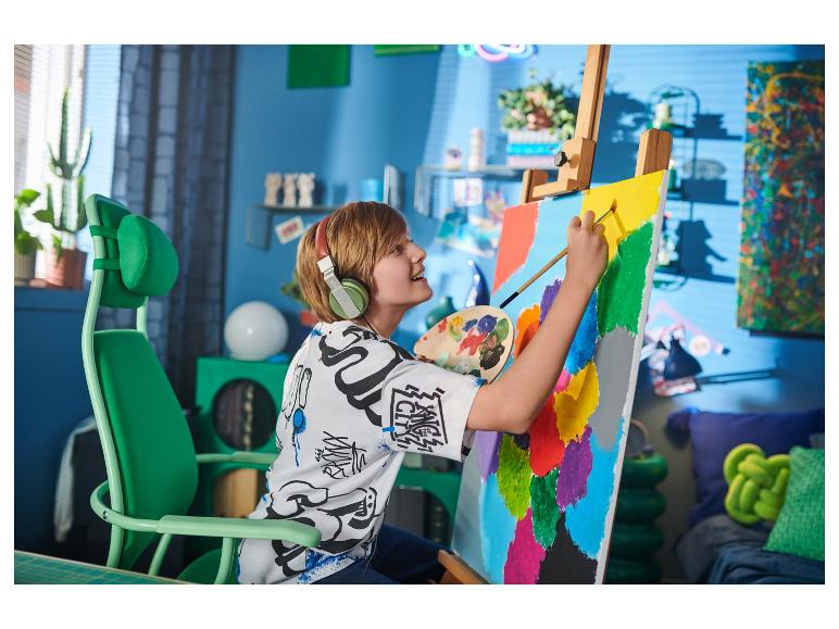 Blonde jongen met koptelefoon schildert op canvas in een groene stoel.