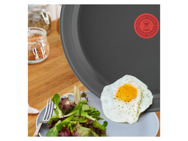 Tefal pan met een gebakken ei en salade op een bord, kruidenpotjes op de achtergrond.