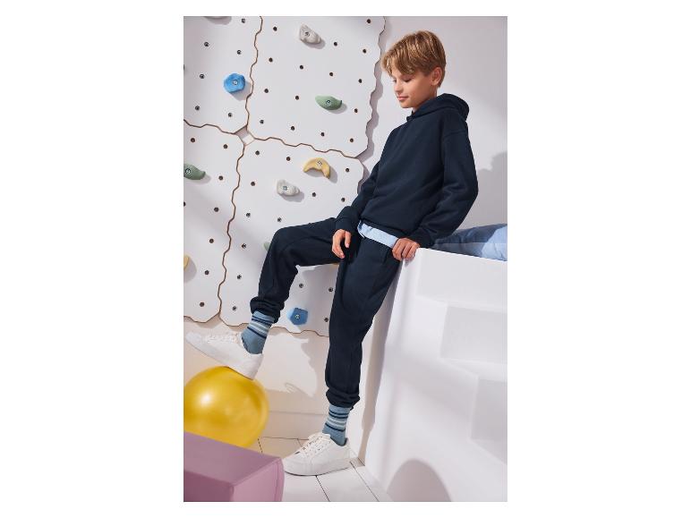 Jongen in marineblauwe hoodie en joggingbroek, met één voet op een gele bal.