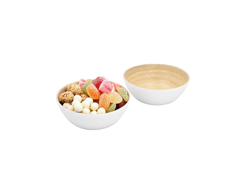 Twee witte kommen, één gevuld met kleurrijke snoepjes en snacks, de andere leeg.