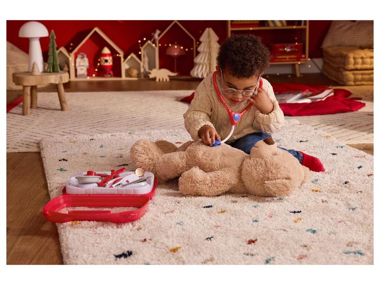 Een kind speelt dokter met een teddybeer en een speelgoed doktersset op een vloerkleed.
