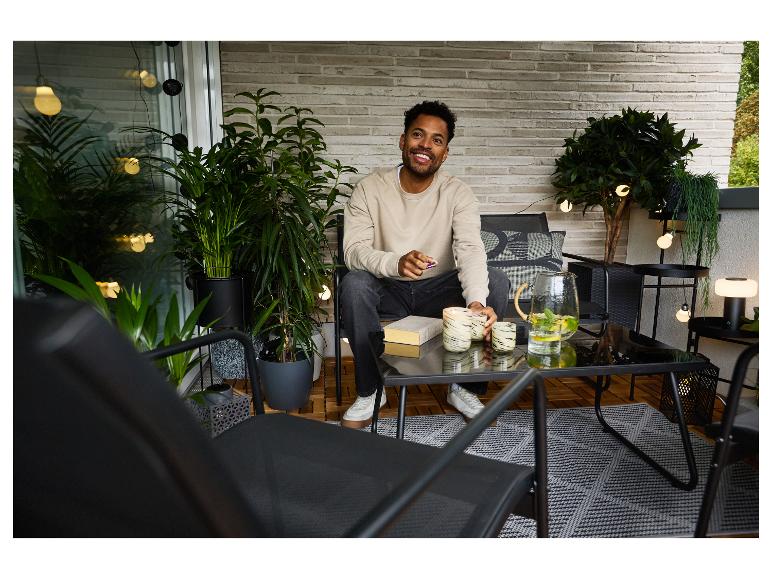 Man op balkon met tuinmeubelen, planten en lichtslingers.
