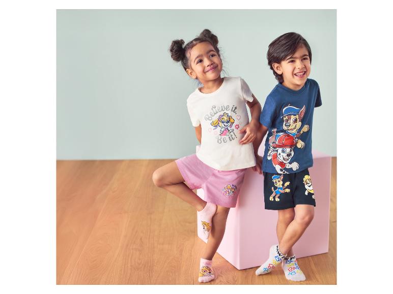 Twee kinderen in Paw Patrol sokken en kleding, lachend voor een roze doos.