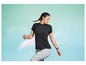 Een vrouw in een zwarte T-shirt en leggings poseert voor een turquoise achtergrond.