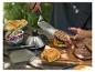 Persoon plaatst burger op broodje met spatel, met barbecue-ingrediënten op tafel.