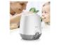 Witte en grijze flessenwarmer met een lachende moeder die een baby voedt op de achtergrond.